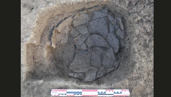 Sur une photo en plan, on aperçoit une fosse dans laquelle se trouve une poterie entière mais cassée.