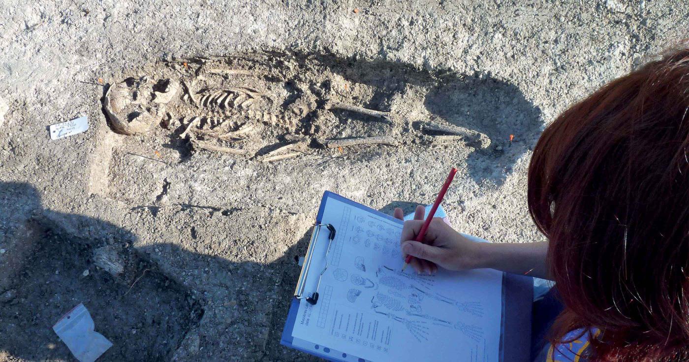 Une archéologue est en train d'éffectuer un relevé de sépulture.