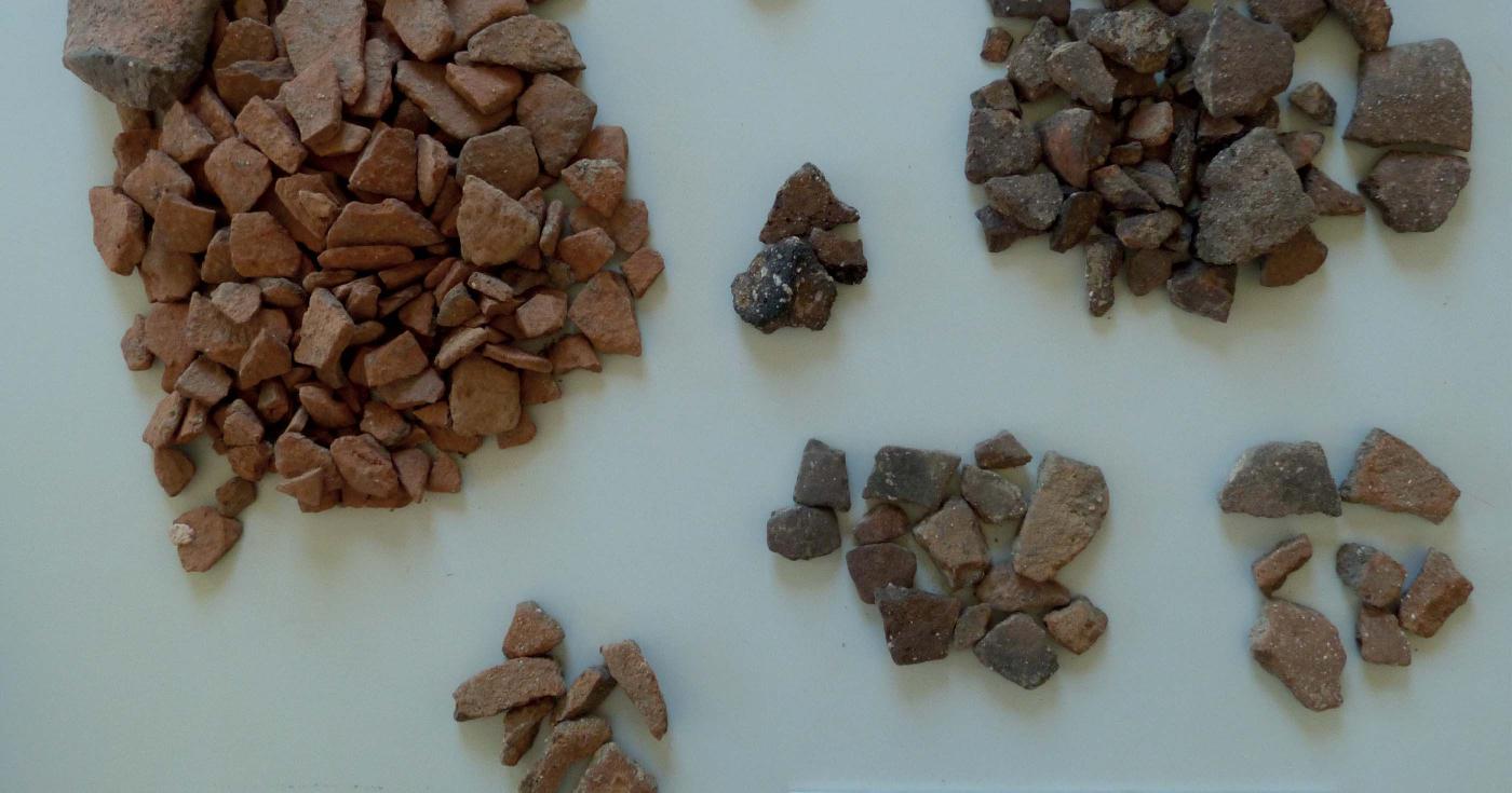 Des fragments de céramique de différents types sont disposés en tas sur une table.