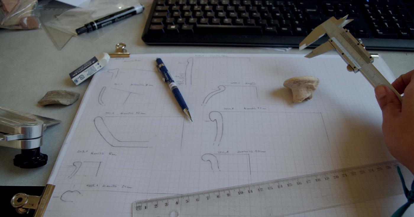 Sur un bureau se trouvent les outils nécessaires au dessin de céramique : conformateur, pied à coulisse, règle, crayon, etc.