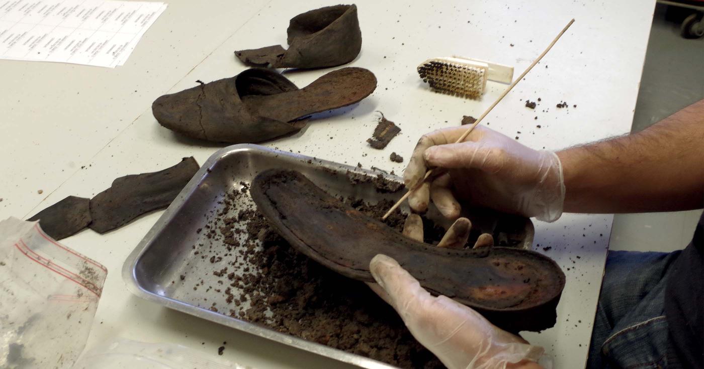 Un archéologue est en train de nettoyer une chaussure d'époque moderne en cuir.