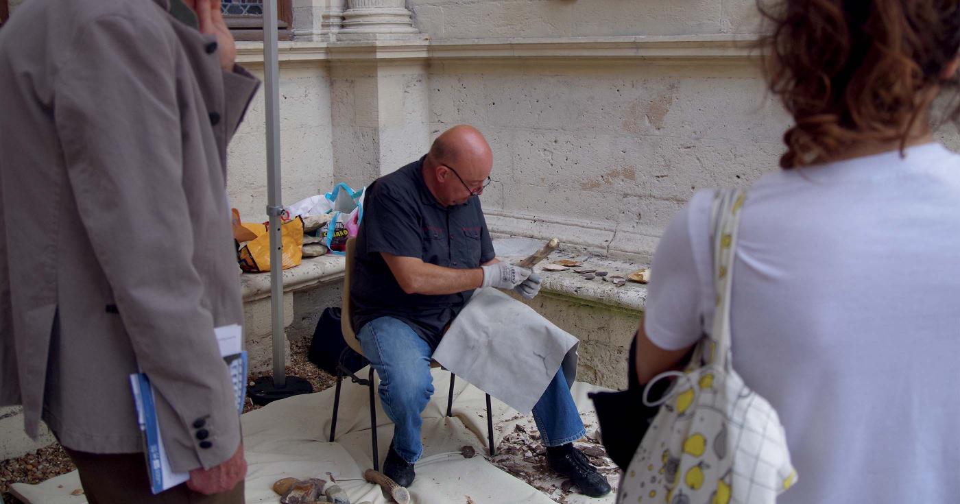 Un homme fait une démonstration de taille de silex davant du public.