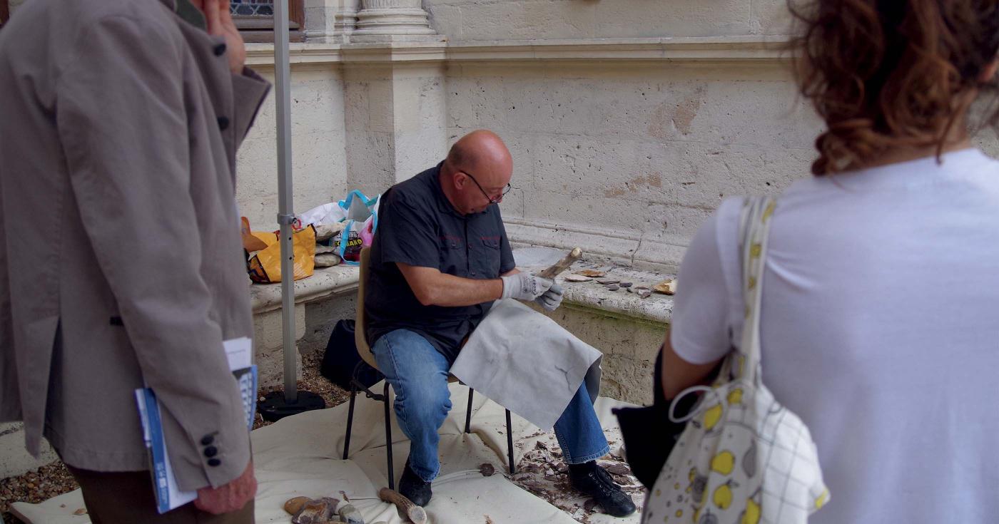 Un homme fait une démonstration de taille de silex davant du public.