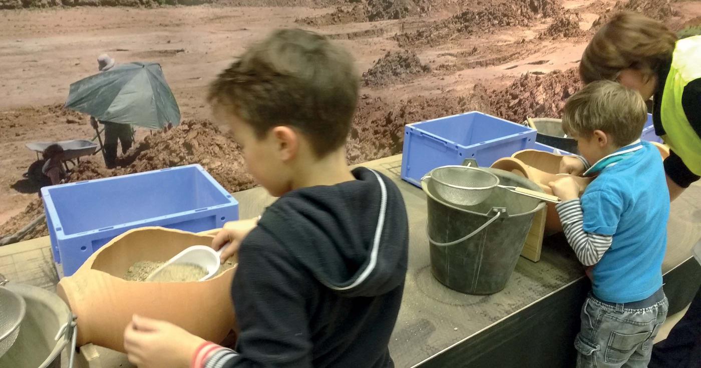 Des enfants participent à un atelier reproduisant une fouille à l'intérieur d'une petite amphore.