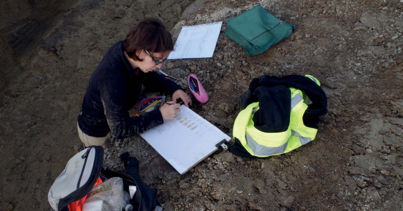 Une archéologue note des informations sur un calque contenant les dessins effectuées sur le terrain.