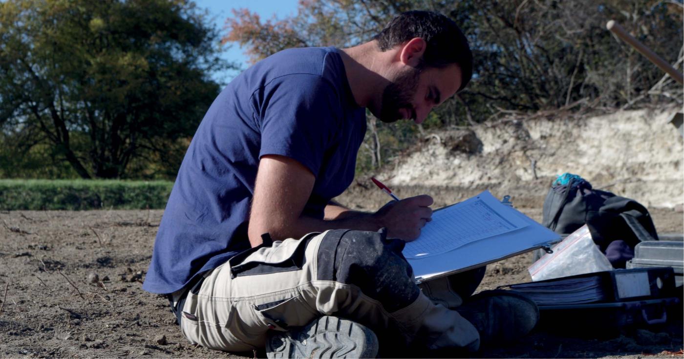 Un archéologue note des informations sur un classeur de terrain.