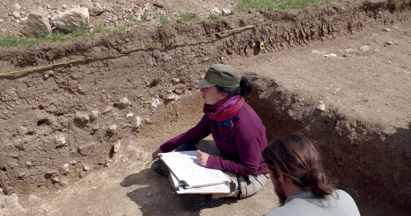 Deux archéologues sont assis devant une coupe stratigraphique pour dessiner et comprendre les différentes couches de sédiment qui la composent.