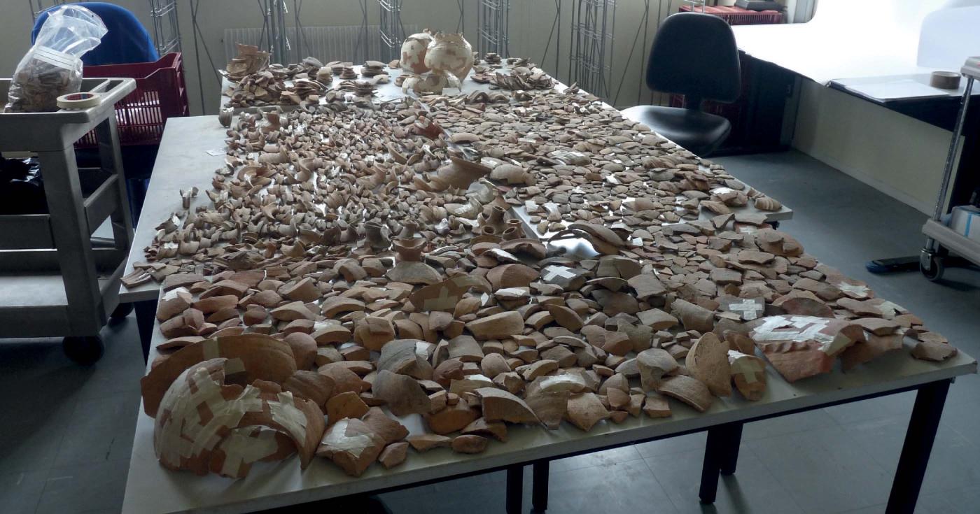 Sur une table d'étude, des centaines de fragments de céramique sont étalés.