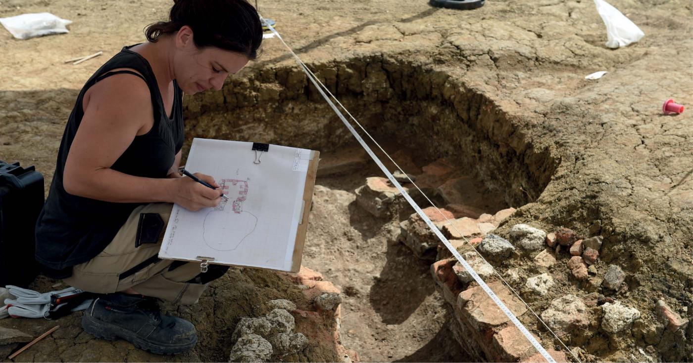 Une archéologue est en train de dessiner des vestiges archéologiques.