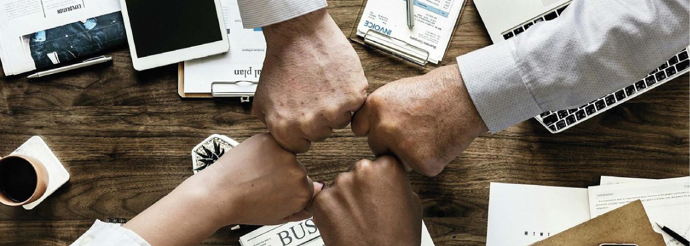 Quatre personnes rejoignent leur main gauche avec le poing fermé, en cercle, comme une équipe de sport le ferait.