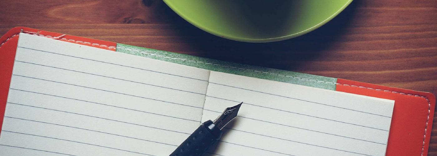 Un feutre est posé sur un cahier à côté d'une tasse de café.